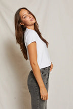 Woman wearing a white midweight tee and high-waisted faded black jeans in a simple studio setting.