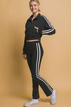Woman wearing a black cropped jacket with white stripes on sleeves paired with matching pants and white sneakers