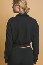 Woman wearing a black sporty jacket with white stripe detail, shown from the back against a beige background