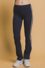 Woman wearing black leggings with white side stripes and white sneakers against a beige background