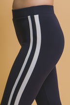 Close-up of navy blue women's leggings with white side stripes on a beige background