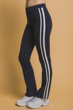 Woman wearing navy leggings with white side stripes paired with white sneakers against beige background
