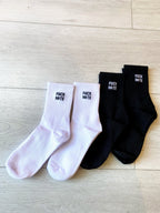 Black and white women's socks with bold statement text, displayed on a light wooden floor background.