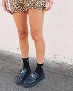 Woman wearing black statement socks and black loafers paired with a leopard print skirt in an urban setting
