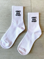 Pair of white women's socks with bold black statement text on ribbed cuffs, laid flat on light wood background
