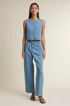 Woman wearing high-waisted wide leg denim pants with front button and pockets in a simple studio setting