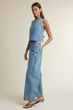 Woman wearing light blue wide-leg denim pants and sleeveless denim top in minimal studio setting
