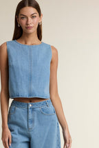 Woman wearing sleeveless light blue denim crop top and matching denim pants against a plain background