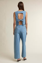 Woman wearing light blue denim sleeveless top with back tie detail and matching wide-leg jeans in a studio setting