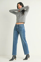 Woman wearing mid-rise straight-leg blue jeans and a fitted gray sweater in a minimalist setting