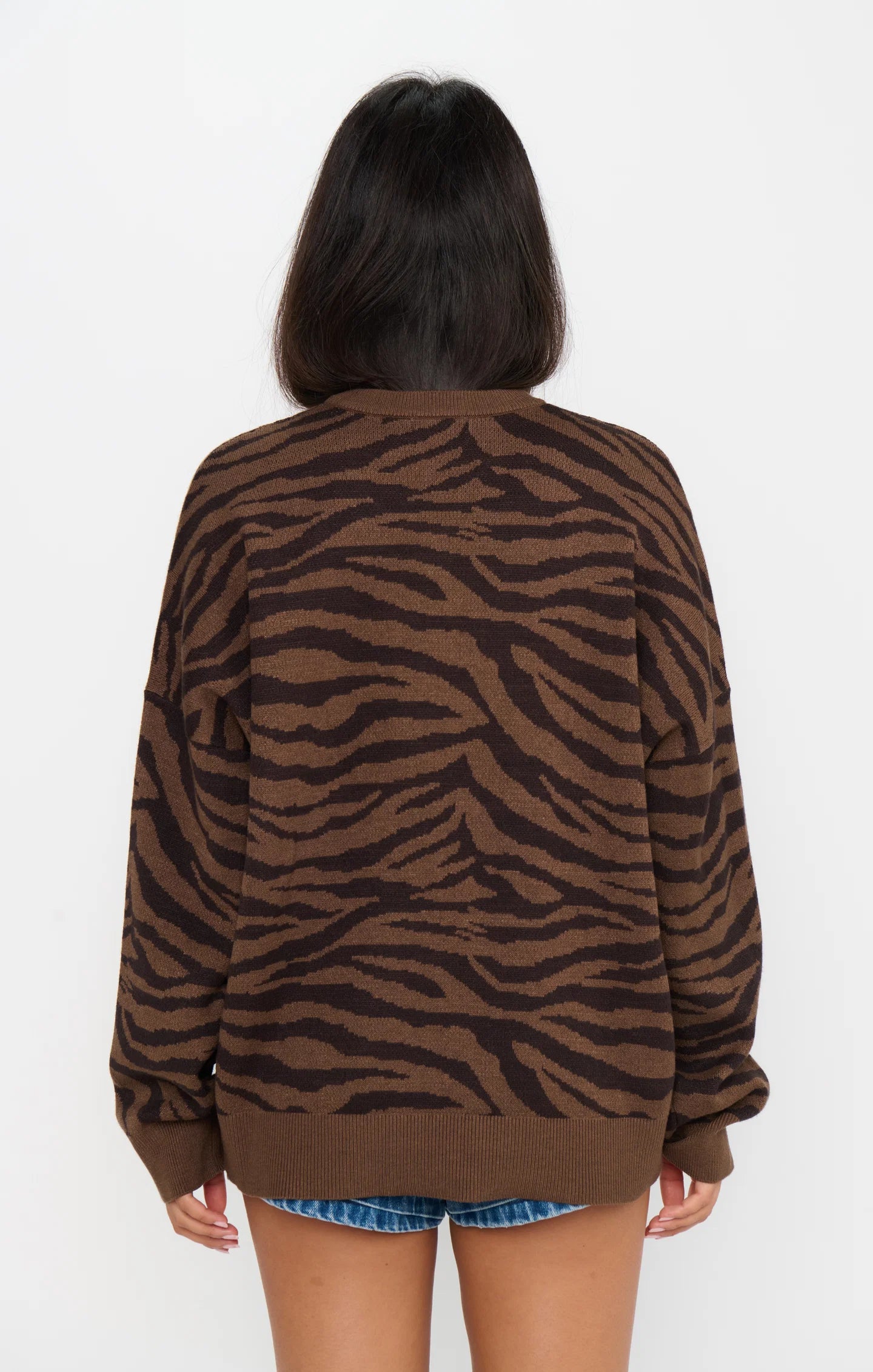 Back view of woman wearing a brown tiger stripe knit sweater with denim shorts