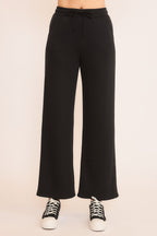 Women's black wide-leg sweatpants with front tie and pockets paired with black and white sneakers