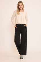 Woman wearing casual black wide-leg pants with pockets and beige long-sleeve top in a relaxed pose