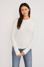 Woman wearing a white ribbed long sleeve top with thumbholes paired with blue jeans on a white background