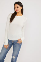 Woman wearing a white ribbed long sleeve top with thumbholes paired with blue distressed jeans against a white background