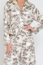 Woman wearing cream-colored flowy pants and matching floral patterned button-up top in brown tones