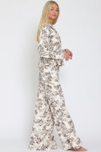 Woman wearing cream and brown floral patterned flowy pants and matching long sleeve top standing against white background