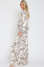 Woman wearing wide-leg toile patterned flowy pants and matching top with long sleeves in neutral tones.