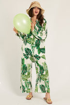 Woman wearing green leaf print long sleeve button down top and matching pants holding a light green balloon