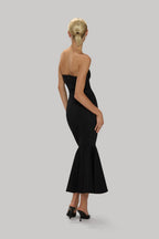 Woman wearing a strapless black trumpet hem dress with a fitted silhouette and flared finish at the bottom.