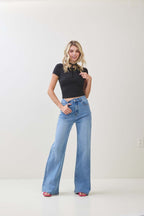 Woman wearing black twist knot cap sleeve top and high-waisted wide-leg blue jeans in a plain room