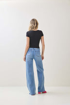 Woman wearing a black short sleeve top and light blue wide-leg jeans standing against a plain background
