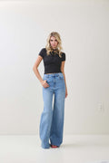 Woman wearing a black twist knot cap sleeve top paired with high-waisted wide-leg blue jeans in women's clothing.