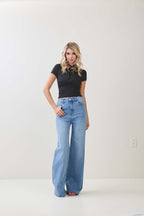 Woman wearing a black twist knot cap sleeve top paired with high-waisted wide-leg blue jeans in women's clothing.