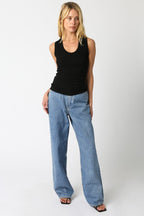 Woman wearing a black ribbed scoop neck sleeveless top paired with wide-leg blue jeans, posing against white background.