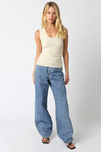 Woman wearing a cream ribbed sleeveless scoop neck top paired with loose light blue denim jeans and black sandals