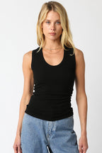 Woman wearing a black ribbed scoop neck sleeveless top paired with light blue denim jeans in a studio setting.