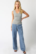 Woman wearing a gray ribbed sleeveless scoop neck top paired with loose-fitting blue jeans and black sandals