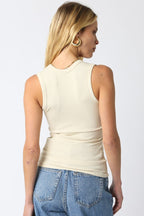 Woman wearing a cream ribbed sleeveless top paired with blue denim jeans in a casual style from the back view