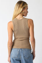 Woman wearing a ribbed sleeveless tan top paired with blue denim jeans, viewed from the back.