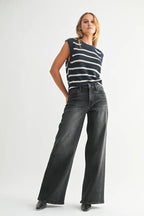 Woman wearing black wide-leg jeans and a sleeveless striped knit top against a white background