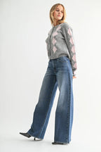 Woman wearing high-rise wide leg blue jeans paired with a gray and pink argyle sweater and black heels