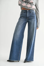 Woman wearing mid-rise wide leg blue jeans paired with a cropped gray sweater, standing against white background