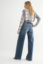 Woman wearing wide leg blue jeans paired with a gray and pink argyle sweater, modeling women's clothing style.