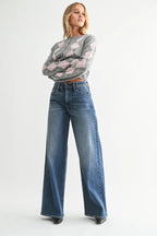 Woman wearing high-rise wide leg blue jeans paired with a gray and pink argyle sweater in a studio setting
