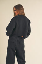 Woman wearing a black cropped fleece sweatshirt and matching black high-waisted cargo pants from behind