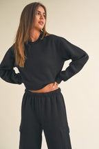 Woman wearing a black cropped fleece sweatshirt paired with matching black cargo pants in a relaxed pose