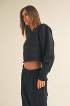 Woman wearing a black cropped fleece sweatshirt and matching black cargo pants in a simple studio setting