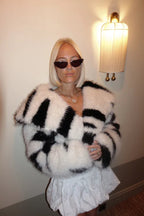 Woman wearing a cropped black and white striped faux fur jacket with sunglasses in a softly lit room