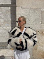 Woman wearing a bold black and white striped faux fur cropped jacket with sunglasses in an outdoor setting