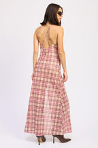 Woman wearing pink plaid sheer maxi dress with crossed spaghetti straps and brown heeled boots, facing away