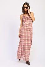 Woman wearing sleeveless pink plaid maxi dress with ruffled neckline and brown pointed boots adjusting sunglasses
