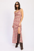 Woman wearing a sleeveless plaid maxi dress with a thigh-high slit and dark knee-high boots in women's clothing style