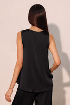 Woman wearing a sleeveless black tank top with a relaxed fit, styled with black pants, shown from the back.