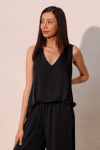 Woman wearing a black sleeveless V-neck tank top styled with a front tuck in casual women's clothing.
