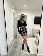 Woman wearing a black cropped jacket and a black and white plaid mini skirt in a modern bedroom mirror selfie